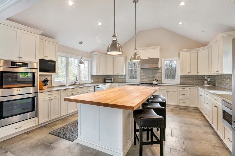 Example of a mid-sized transitional u-shaped porcelain tile eat-in kitchen design in New York with an undermount sink, recessed-panel cabinets, white cabinets, wood countertops, gray backsplash, subway tile backsplash, stainless steel appliances and an island