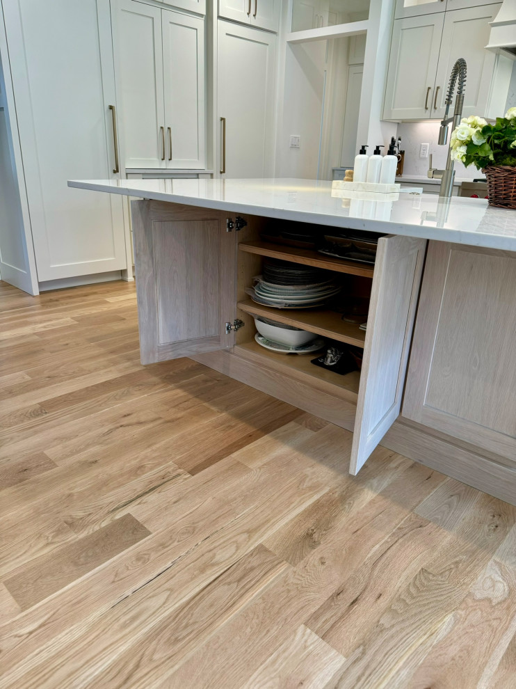 Example of a mid-sized transitional l-shaped light wood floor, brown floor and wallpaper ceiling eat-in kitchen design in Atlanta with a farmhouse sink, shaker cabinets, white cabinets, granite countertops, white backsplash, stainless steel appliances, an island and white countertops