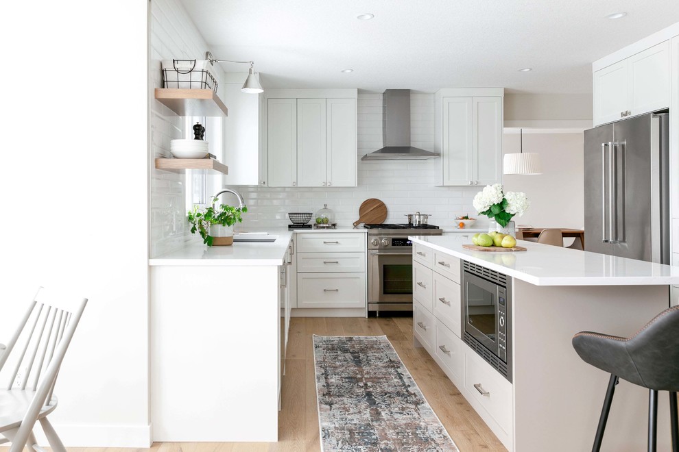 Example of a large transitional u-shaped medium tone wood floor and brown floor eat-in kitchen design in Calgary with an undermount sink, shaker cabinets, white cabinets, quartzite countertops, white backsplash, subway tile backsplash, stainless steel appliances, an island and white countertops