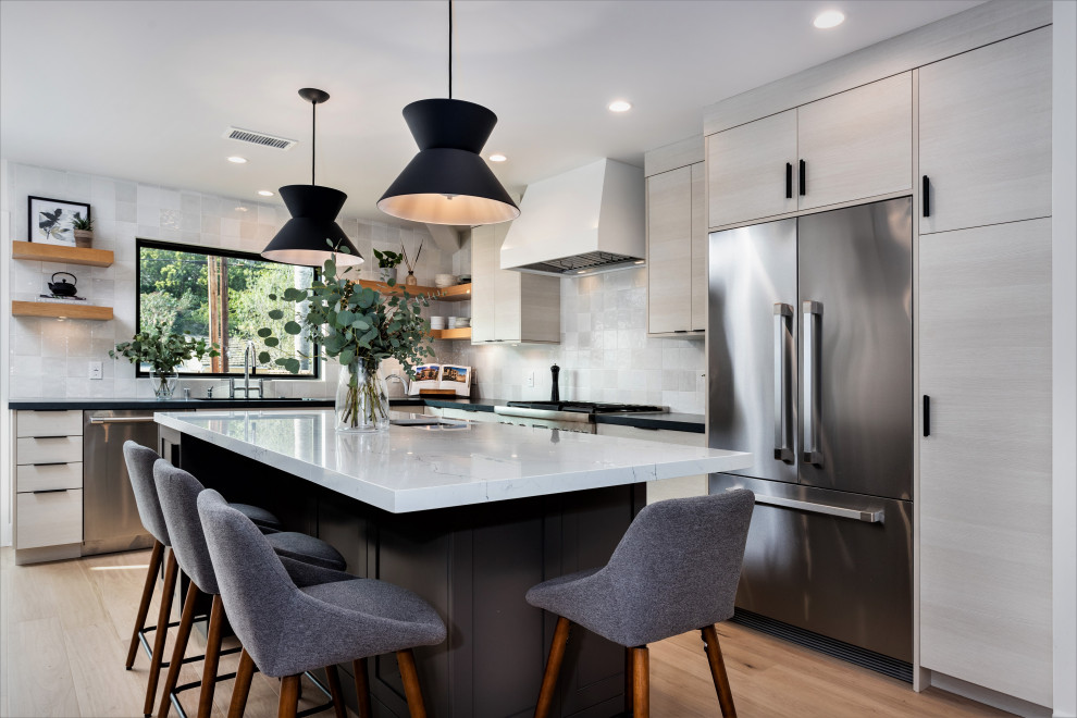Inspiration for a small scandinavian l-shaped eat-in kitchen in Los Angeles with an undermount sink, flat-panel cabinets, white cabinets, quartz benchtops, white splashback, stainless steel appliances, light hardwood floors, with island and black benchtop.