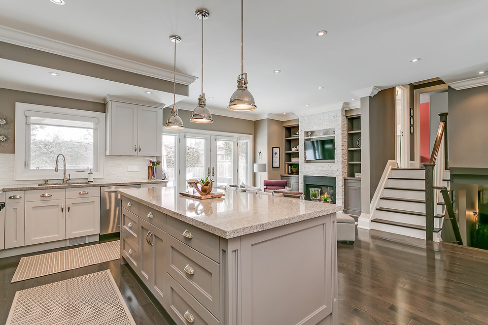 Open concept kitchen - mid-sized transitional l-shaped dark wood floor and brown floor open concept kitchen idea in Toronto with an undermount sink, recessed-panel cabinets, white cabinets, quartz countertops, white backsplash, matchstick tile backsplash, stainless steel appliances, an island and multicolored countertops