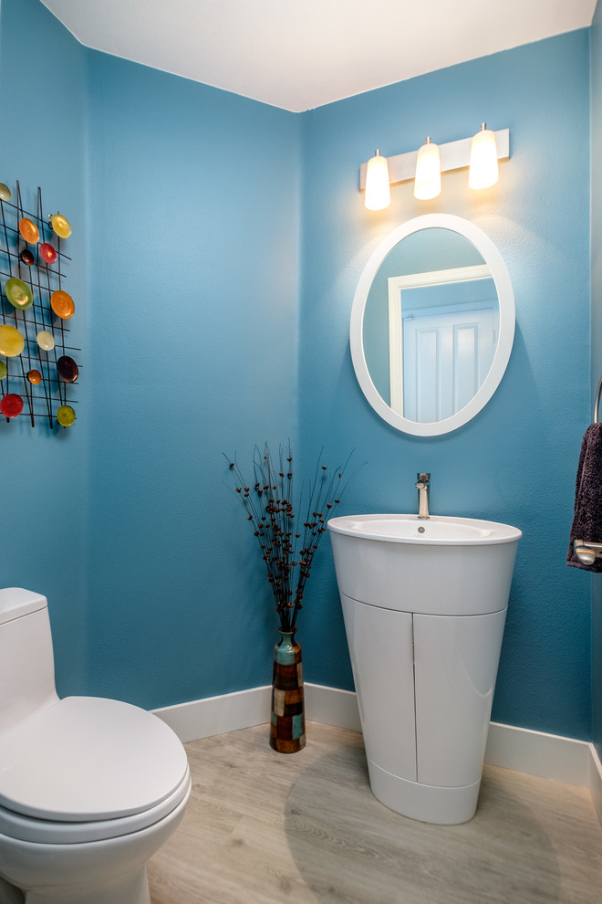 This is an example of a transitional powder room in Orange County with blue walls, light hardwood floors, a pedestal sink and beige floor.