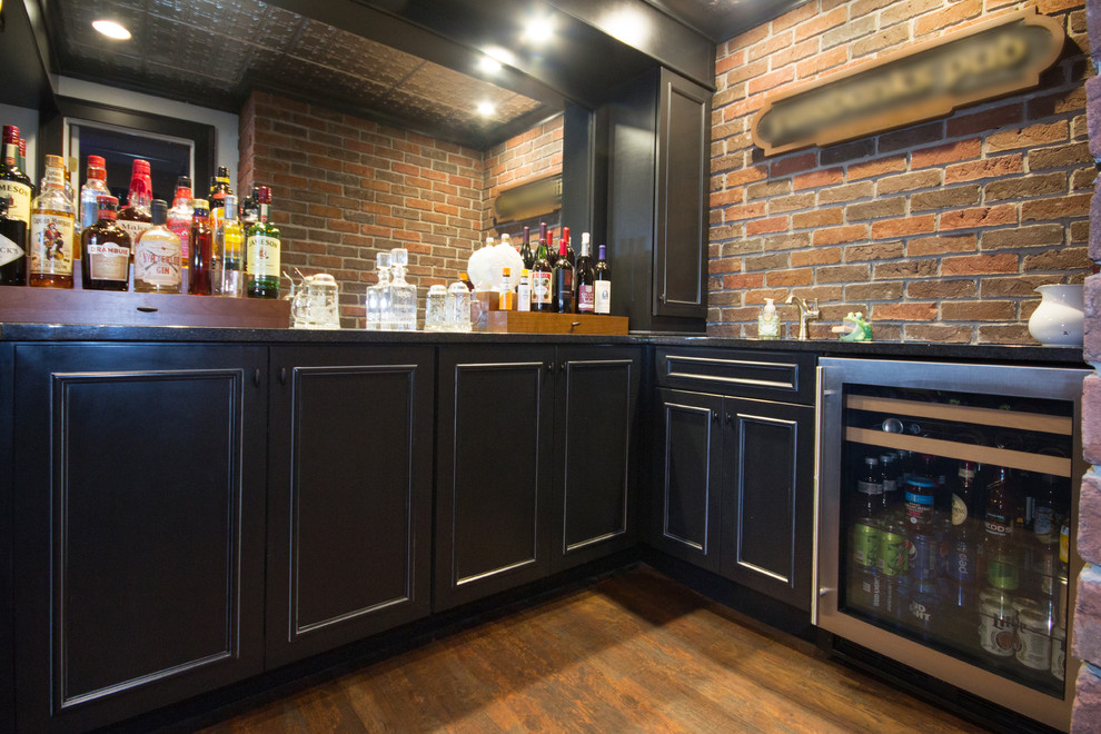 Inspiration for a small traditional u-shaped seated home bar in Grand Rapids with an undermount sink, black cabinets, granite benchtops, brown splashback, brick splashback, medium hardwood floors, brown floor and raised-panel cabinets.