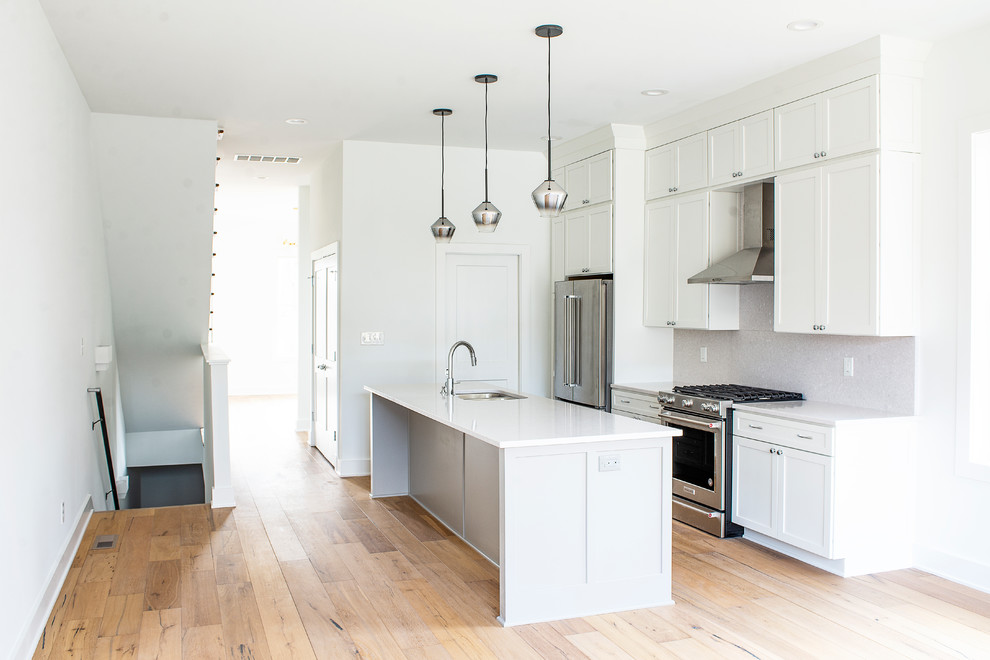 This is an example of a mid-sized contemporary single-wall eat-in kitchen in Indianapolis with an undermount sink, shaker cabinets, white cabinets, quartz benchtops, white splashback, stone slab splashback, stainless steel appliances, light hardwood floors, with island, brown floor and white benchtop.