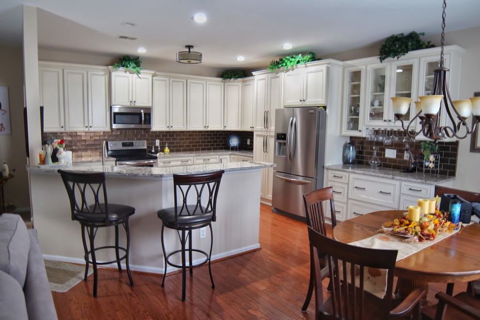 Mid-sized u-shaped medium tone wood floor and brown floor kitchen photo in Charleston with an undermount sink, raised-panel cabinets, beige cabinets, granite countertops, brown backsplash, ceramic backsplash, stainless steel appliances and beige countertops