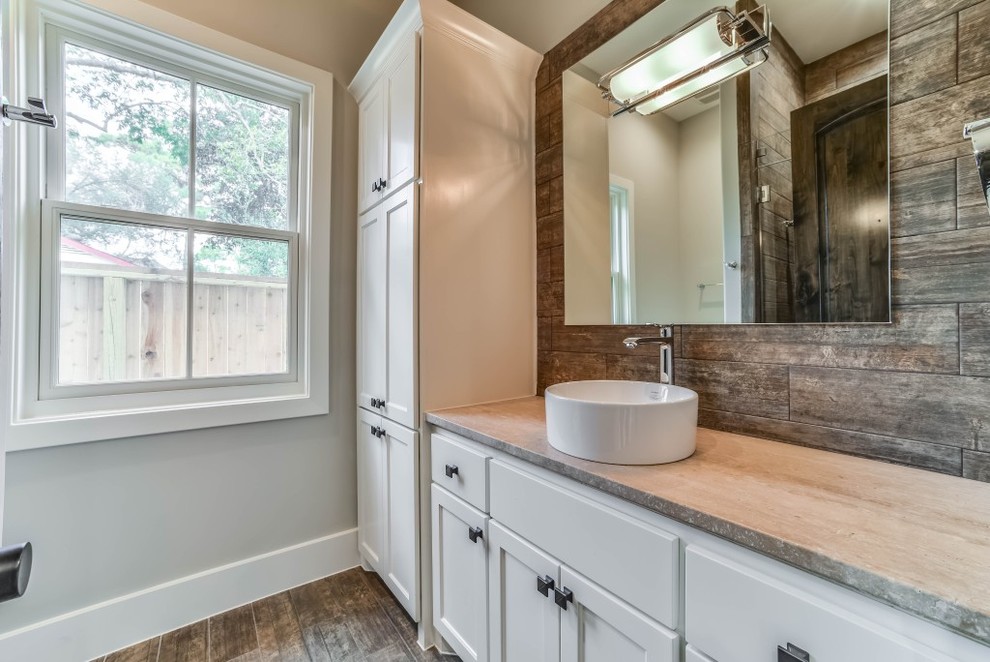 Photo of a transitional powder room in Houston with recessed-panel cabinets, white cabinets, porcelain tile, grey walls, porcelain floors, a vessel sink, limestone benchtops and brown floor.