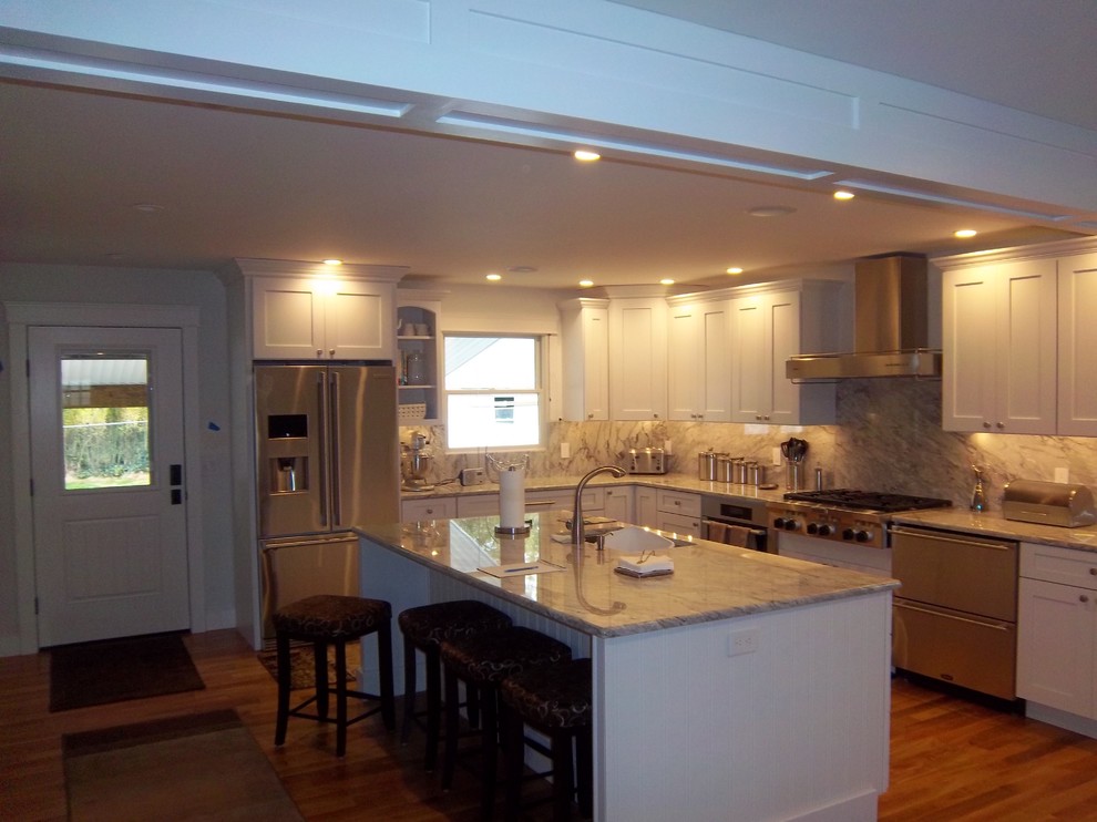 Open concept kitchen - mid-sized transitional l-shaped medium tone wood floor and brown floor open concept kitchen idea with an undermount sink, recessed-panel cabinets, white cabinets, granite countertops, gray backsplash, stone slab backsplash, stainless steel appliances and an island