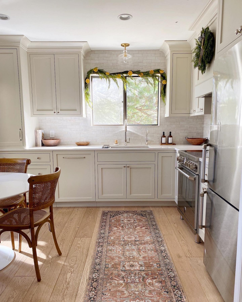 Inspiration for a mid-sized modern l-shaped eat-in kitchen in New York with a drop-in sink, recessed-panel cabinets, white cabinets, granite benchtops, white splashback, ceramic splashback, stainless steel appliances, light hardwood floors, no island, multi-coloured floor, white benchtop and vaulted.