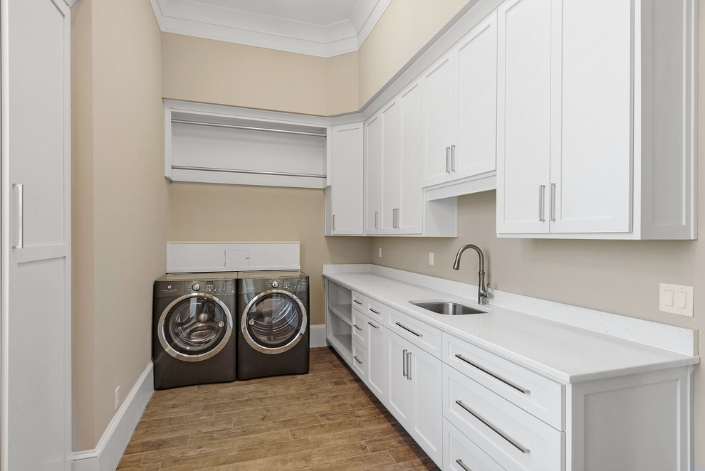 Large traditional single-wall dedicated laundry room in Miami with an undermount sink, shaker cabinets, white cabinets, marble benchtops, beige walls, medium hardwood floors, a side-by-side washer and dryer and beige floor.