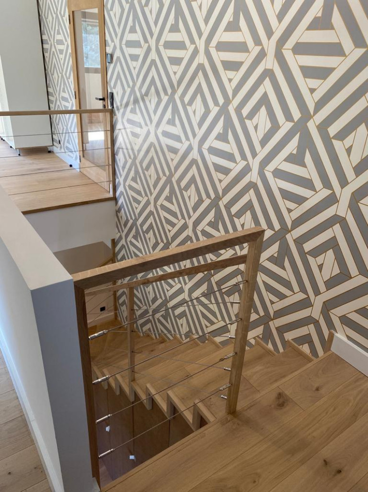 Cette photo montre un escalier tendance en L avec des marches en bois, des contremarches en bois, un garde-corps en câble et du papier peint.