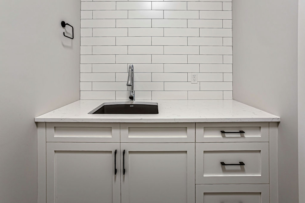 Laundry room - transitional laundry room idea in Calgary with an undermount sink, shaker cabinets, white cabinets, quartz countertops, white backsplash, ceramic backsplash, white walls and white countertops
