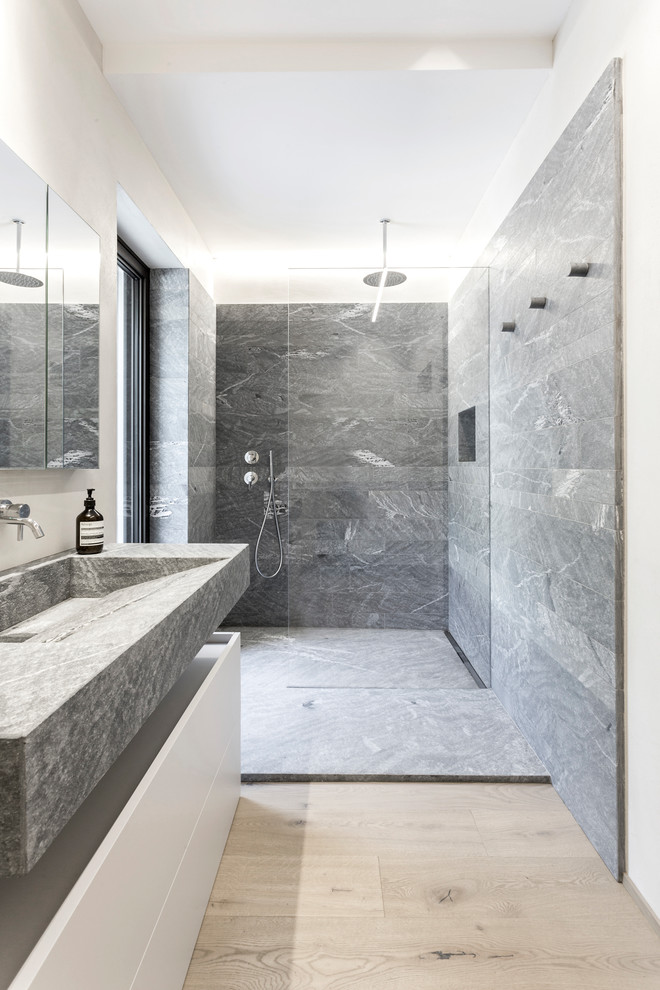Photo of a modern bathroom in Other with flat-panel cabinets, white cabinets, an alcove shower, gray tile, white walls, light hardwood floors, a trough sink, beige floor, an open shower and grey benchtops.
