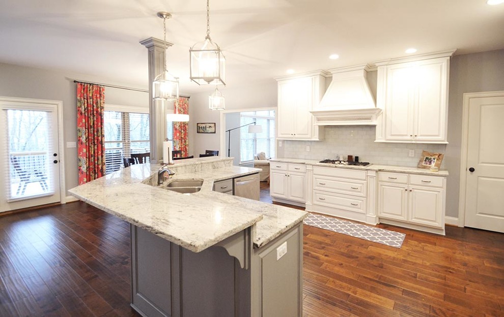 Mid-sized transitional l-shaped open plan kitchen in Louisville with a double-bowl sink, raised-panel cabinets, white cabinets, granite benchtops, white splashback, porcelain splashback, stainless steel appliances, medium hardwood floors, with island, brown floor and white benchtop.