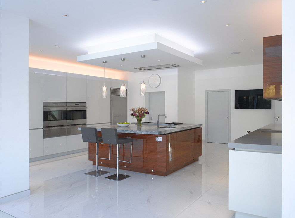 Large contemporary eat-in kitchen in London with flat-panel cabinets, white cabinets, marble benchtops, grey splashback, glass sheet splashback, stainless steel appliances, ceramic floors, with island, white floor and grey benchtop.