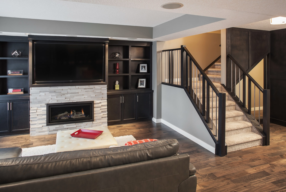 Inspiration for a mid-sized contemporary basement in Calgary with grey walls, dark hardwood floors, a standard fireplace, a stone fireplace surround and brown floor.