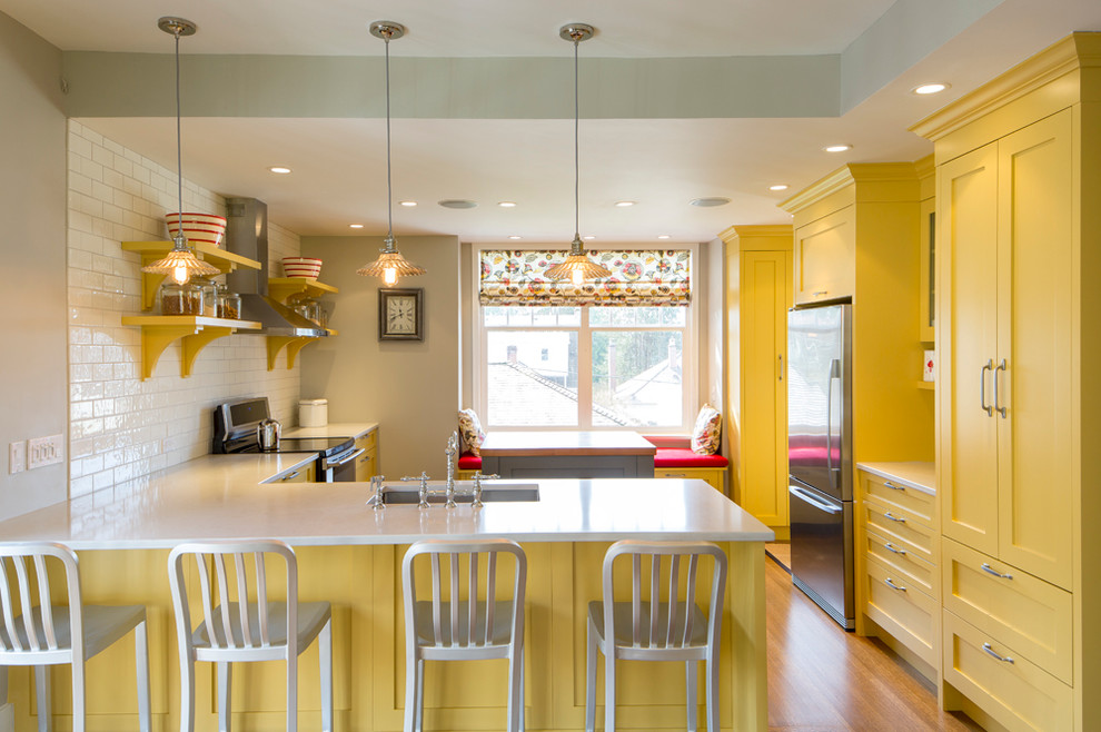 This is an example of a mid-sized traditional u-shaped open plan kitchen in Vancouver with shaker cabinets, yellow cabinets, quartz benchtops, white splashback, stainless steel appliances, medium hardwood floors, an undermount sink, subway tile splashback, with island and brown floor.