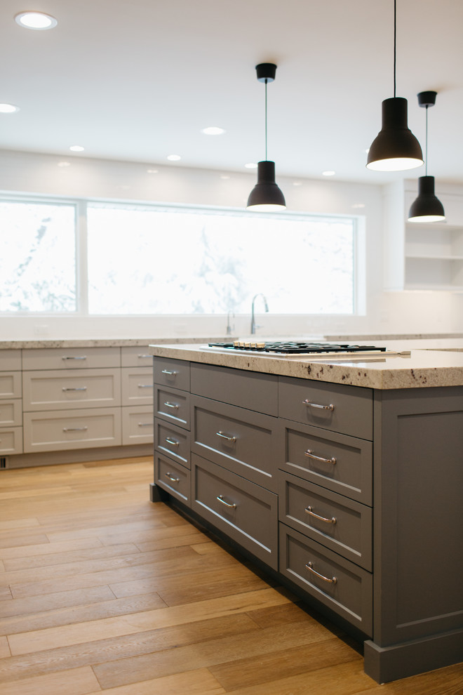 Inspiration for a mid-sized transitional l-shaped open plan kitchen in Seattle with a farmhouse sink, shaker cabinets, grey cabinets, granite benchtops, white splashback, subway tile splashback, panelled appliances, light hardwood floors and with island.