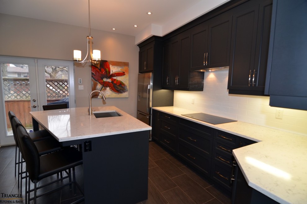 Example of a mid-sized transitional single-wall kitchen design in Ottawa with an undermount sink, shaker cabinets, black cabinets, quartzite countertops, white backsplash, subway tile backsplash, stainless steel appliances and an island