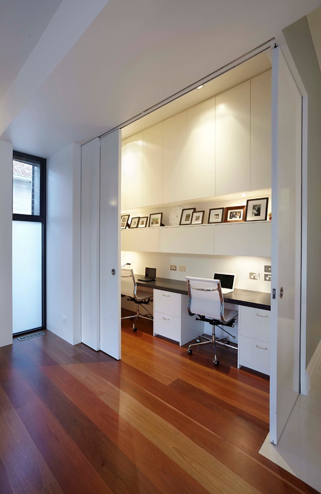 Small contemporary study room in Melbourne with white walls, medium hardwood floors, a built-in desk and brown floor.