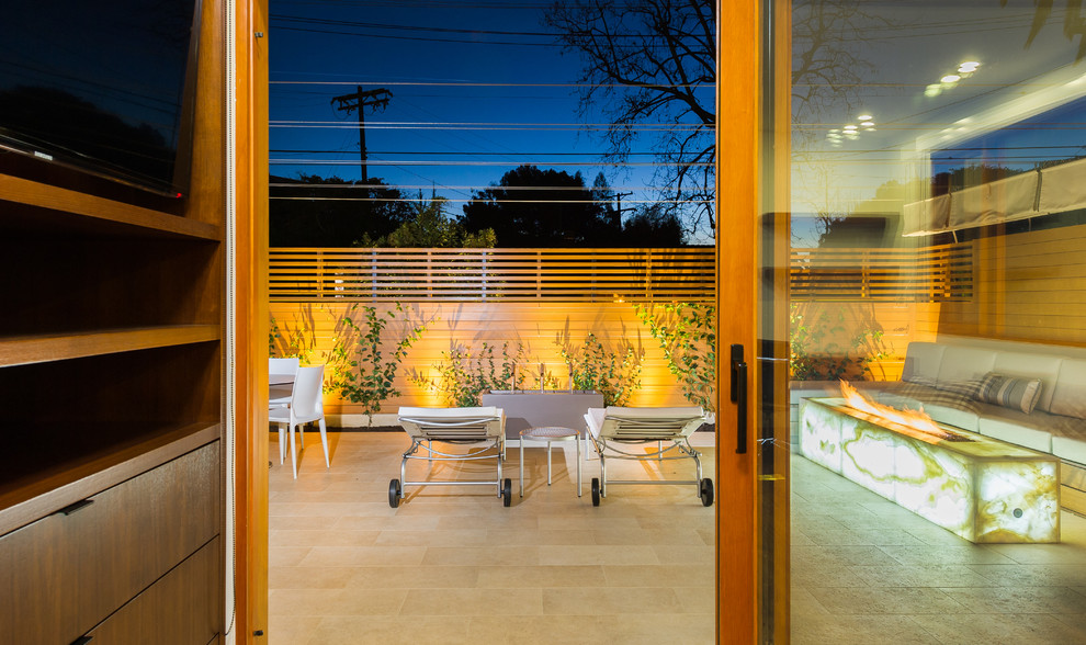 Photo of a mid-sized modern patio in Los Angeles with a fire feature, tile and an awning.