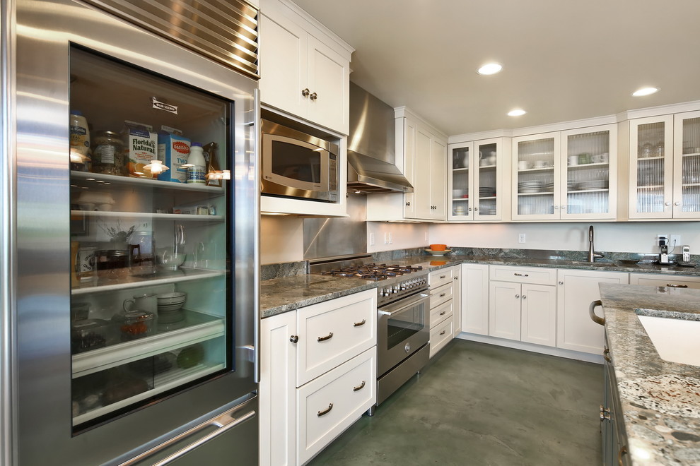 Beach style u-shaped kitchen in Seattle with an undermount sink, glass-front cabinets, white cabinets, granite benchtops, grey splashback, stone slab splashback, stainless steel appliances, concrete floors, a peninsula, green floor and grey benchtop.