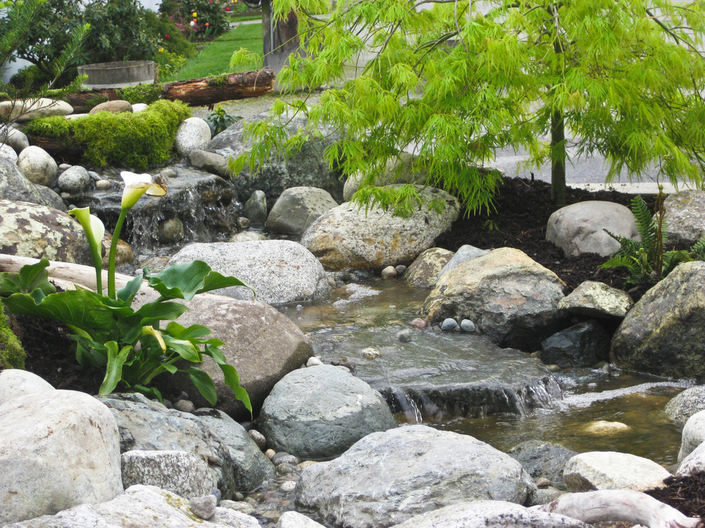 This is an example of a mid-sized rustic full sun backyard stone water fountain landscape in Seattle for spring.