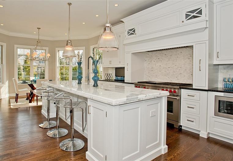 Example of a mid-sized transitional single-wall medium tone wood floor and beige floor eat-in kitchen design in Chicago with shaker cabinets, white cabinets, marble countertops, beige backsplash, porcelain backsplash, white appliances and an island