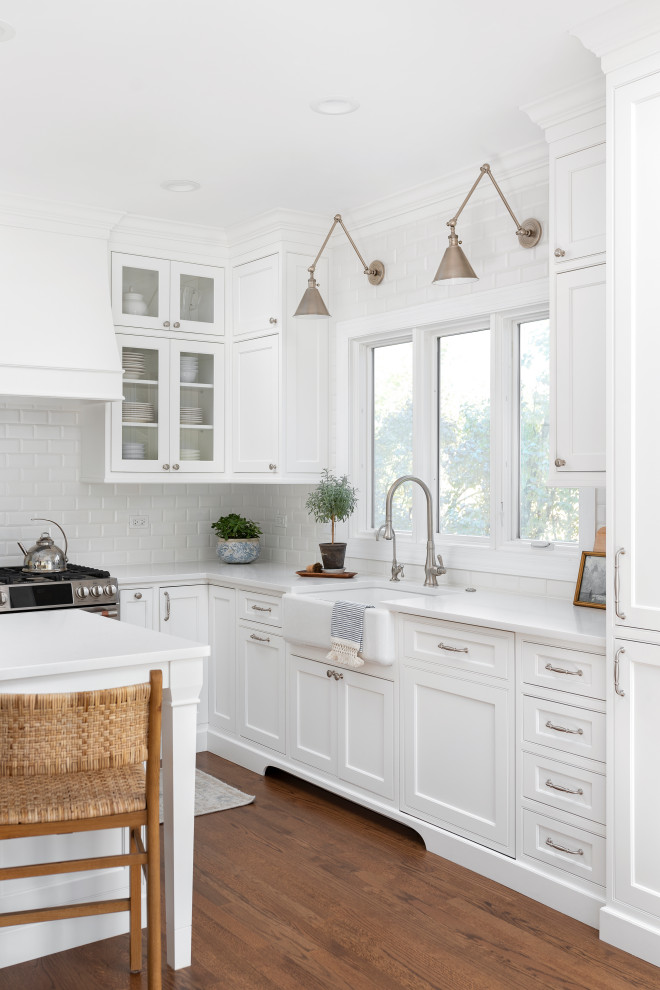 Example of a mid-sized transitional l-shaped medium tone wood floor and brown floor eat-in kitchen design in Chicago with a farmhouse sink, beaded inset cabinets, white cabinets, quartz countertops, white backsplash, ceramic backsplash, paneled appliances, an island and white countertops