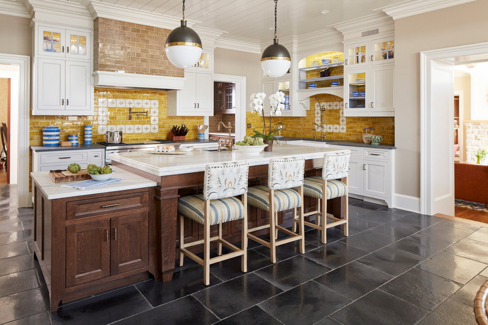 Photo of a country l-shaped eat-in kitchen in New York with a farmhouse sink, shaker cabinets, white cabinets, yellow splashback, stainless steel appliances and with island.