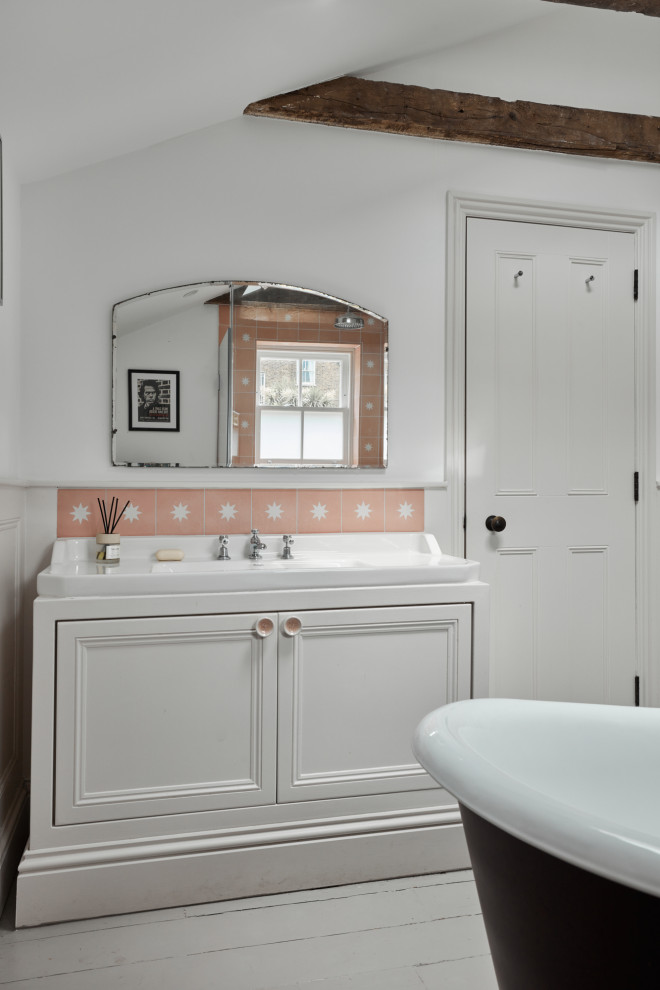 This is an example of a small eclectic kids bathroom in London with recessed-panel cabinets, beige cabinets, a freestanding tub, an open shower, a wall-mount toilet, pink tile, cement tile, white walls, painted wood floors, an undermount sink, grey floor, a hinged shower door, white benchtops, a niche, a single vanity, a freestanding vanity, exposed beam and panelled walls.