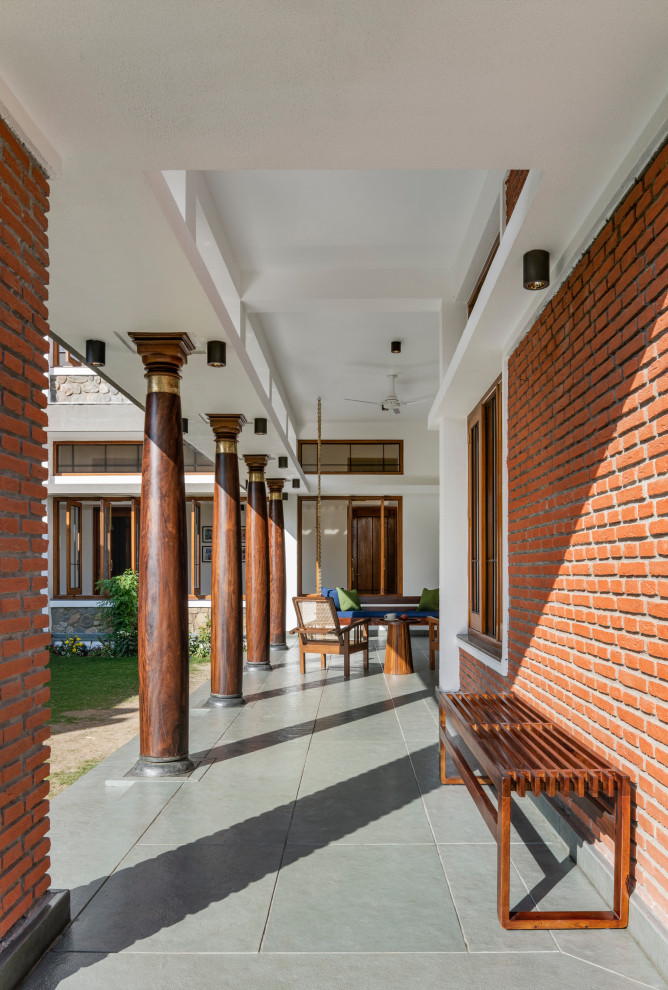 Inspiration for a large contemporary front yard verandah in Chennai with with columns, natural stone pavers, a roof extension and mixed railing.