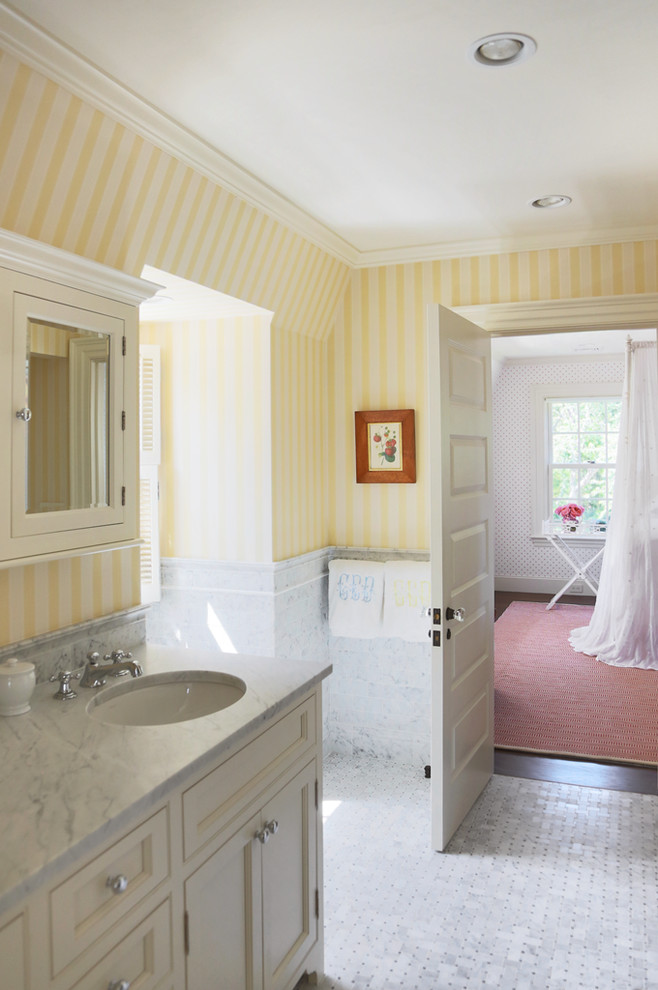 This is an example of a mid-sized beach style bathroom in Boston with an undermount sink, beaded inset cabinets, white cabinets, marble benchtops, yellow walls and mosaic tile floors.