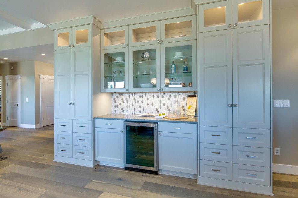 Design ideas for a mid-sized arts and crafts l-shaped open plan kitchen with an undermount sink, recessed-panel cabinets, grey cabinets, quartz benchtops, white splashback, ceramic splashback, stainless steel appliances, medium hardwood floors, with island, brown floor and grey benchtop.