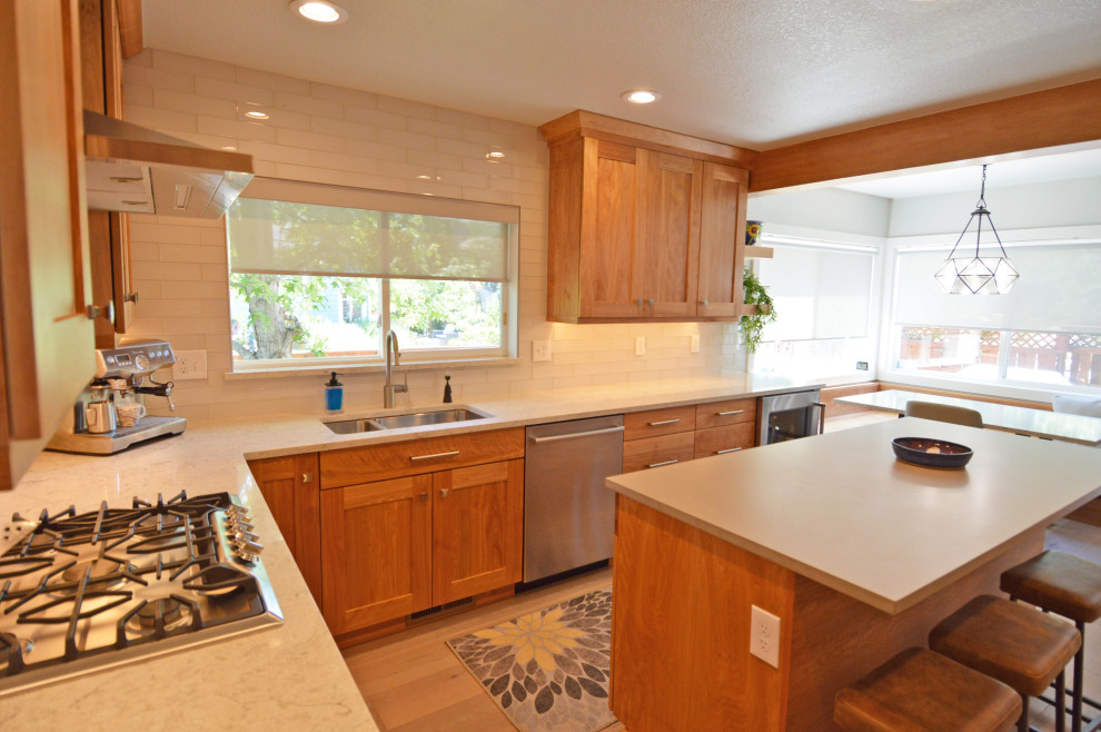 Photo of a mid-sized transitional u-shaped eat-in kitchen in Denver with an undermount sink, shaker cabinets, medium wood cabinets, quartz benchtops, white splashback, glass tile splashback, stainless steel appliances, light hardwood floors, with island, grey floor, multi-coloured benchtop and exposed beam.