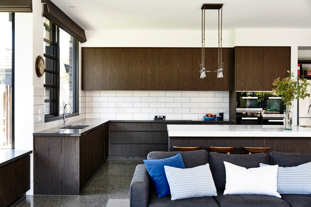 Design ideas for a large contemporary l-shaped open plan kitchen in Melbourne with a double-bowl sink, flat-panel cabinets, dark wood cabinets, solid surface benchtops, white splashback, ceramic splashback, stainless steel appliances, with island and concrete floors.