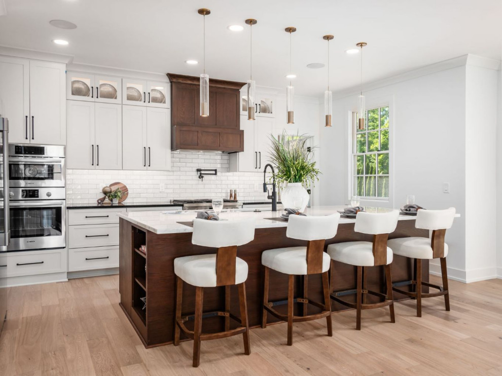 Large transitional l-shaped light wood floor and brown floor eat-in kitchen photo in Columbus with an undermount sink, flat-panel cabinets, white cabinets, quartz countertops, white backsplash, ceramic backsplash, stainless steel appliances, an island and black countertops