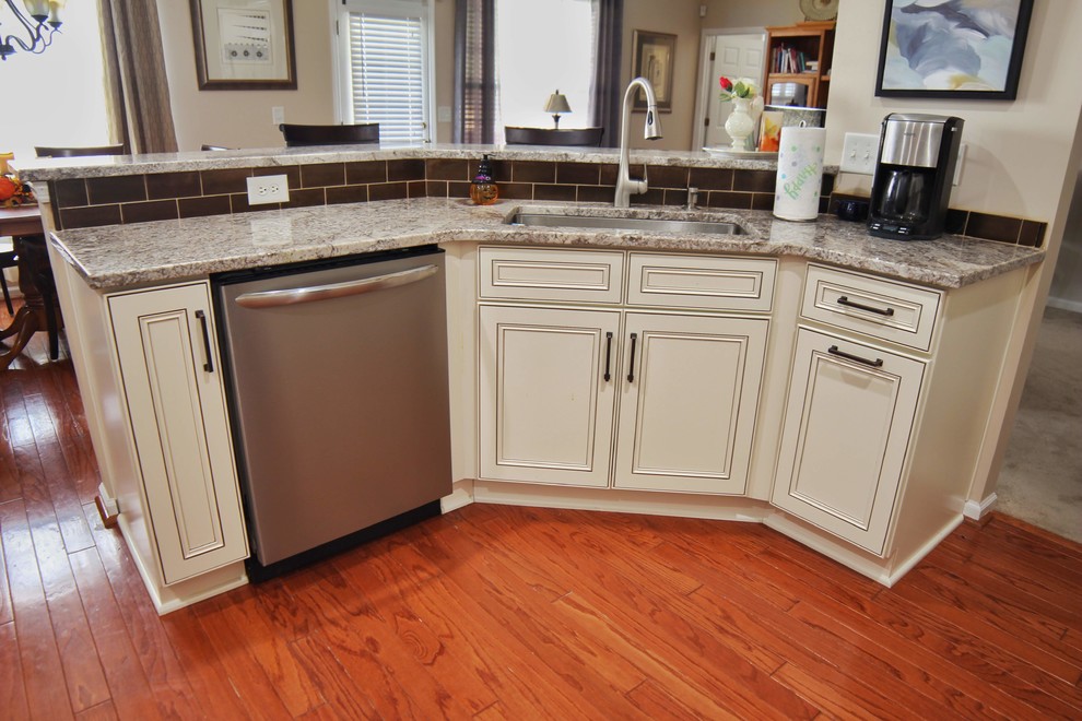 Example of a mid-sized u-shaped medium tone wood floor and brown floor kitchen design in Charleston with an undermount sink, raised-panel cabinets, beige cabinets, granite countertops, brown backsplash, ceramic backsplash, stainless steel appliances and beige countertops