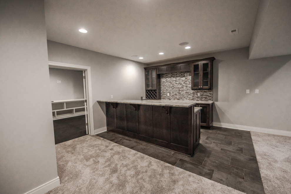 Cette photo montre un grand sous-sol chic semi-enterré avec un bar de salon, un mur gris, moquette et un sol marron.