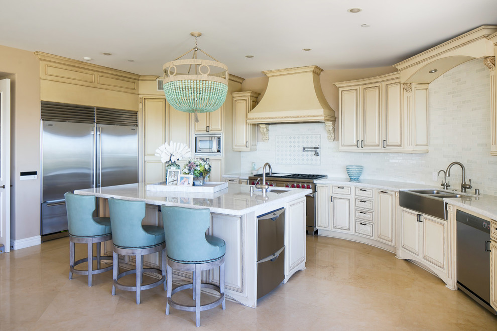 Beach style kitchen in Orange County with a farmhouse sink, raised-panel cabinets, beige cabinets, white splashback, subway tile splashback, stainless steel appliances and with island.
