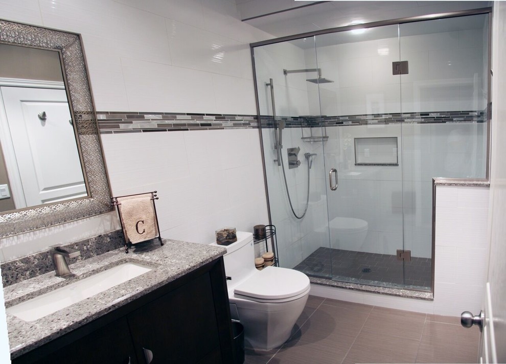Mid-sized transitional 3/4 gray tile, white tile and porcelain tile porcelain tile and brown floor alcove shower photo with flat-panel cabinets, black cabinets, a one-piece toilet, white walls, an undermount sink, granite countertops, a hinged shower door and gray countertops