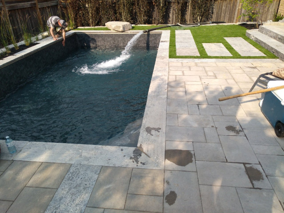 This is an example of a small contemporary backyard rectangular pool in Toronto with a water feature and natural stone pavers.