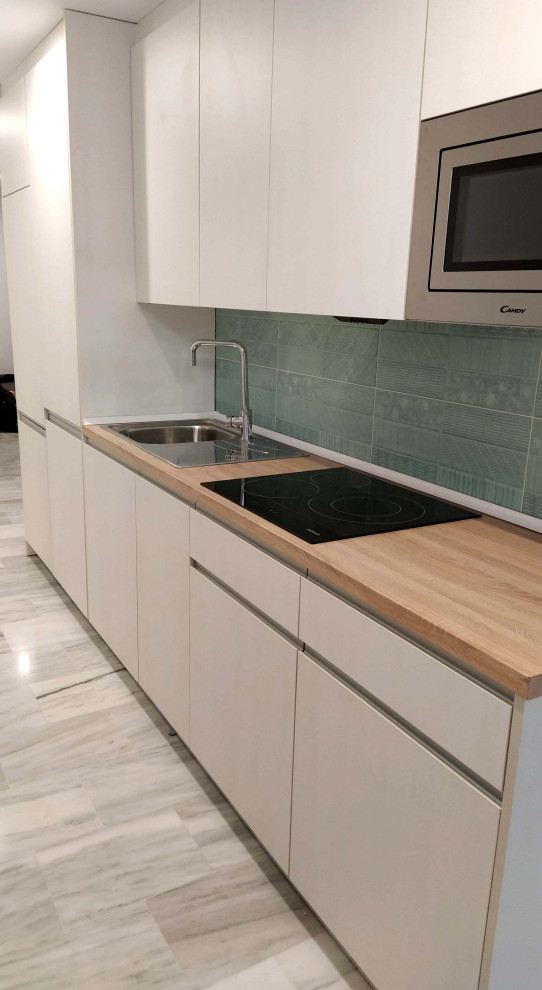 Small scandinavian single-wall open plan kitchen in Malaga with a single-bowl sink, flat-panel cabinets, white cabinets, wood benchtops, green splashback, ceramic splashback, stainless steel appliances, marble floors, no island, grey floor and brown benchtop.