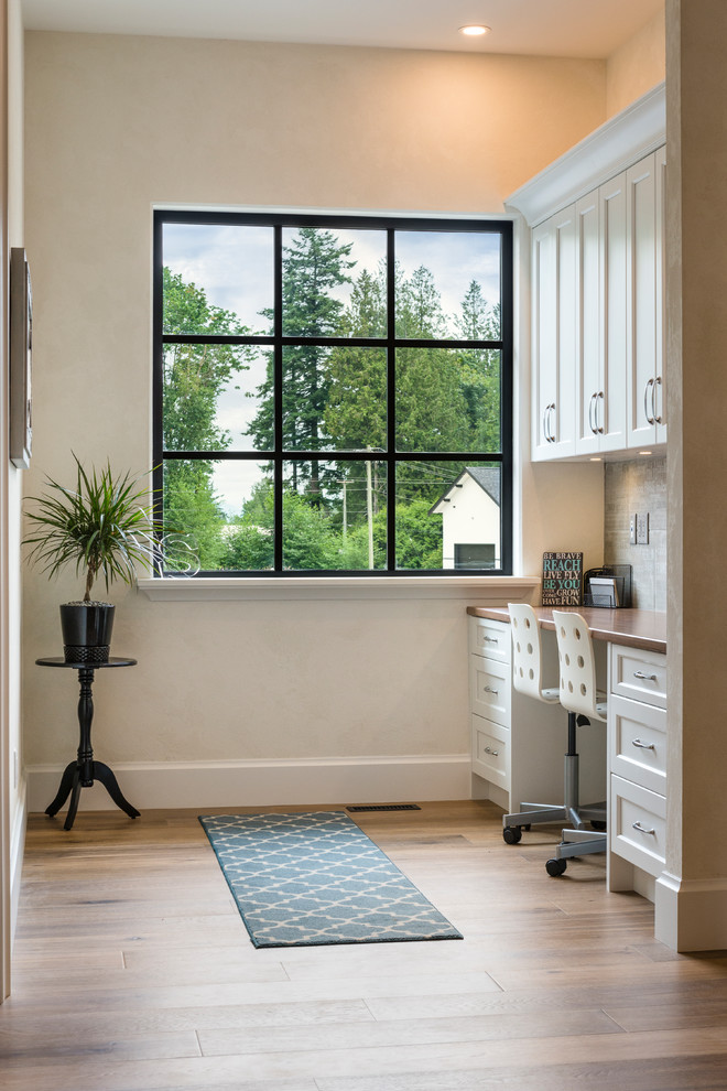 Photo of a mid-sized mediterranean study room in Vancouver with white walls, medium hardwood floors, a built-in desk and brown floor.