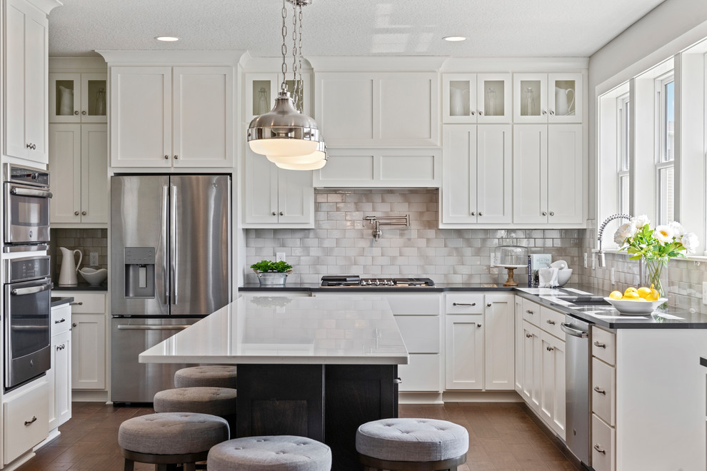 Photo of an expansive traditional u-shaped kitchen in Minneapolis with an undermount sink, shaker cabinets, quartzite benchtops, grey splashback, subway tile splashback, stainless steel appliances, medium hardwood floors, with island, white cabinets, brown floor and black benchtop.