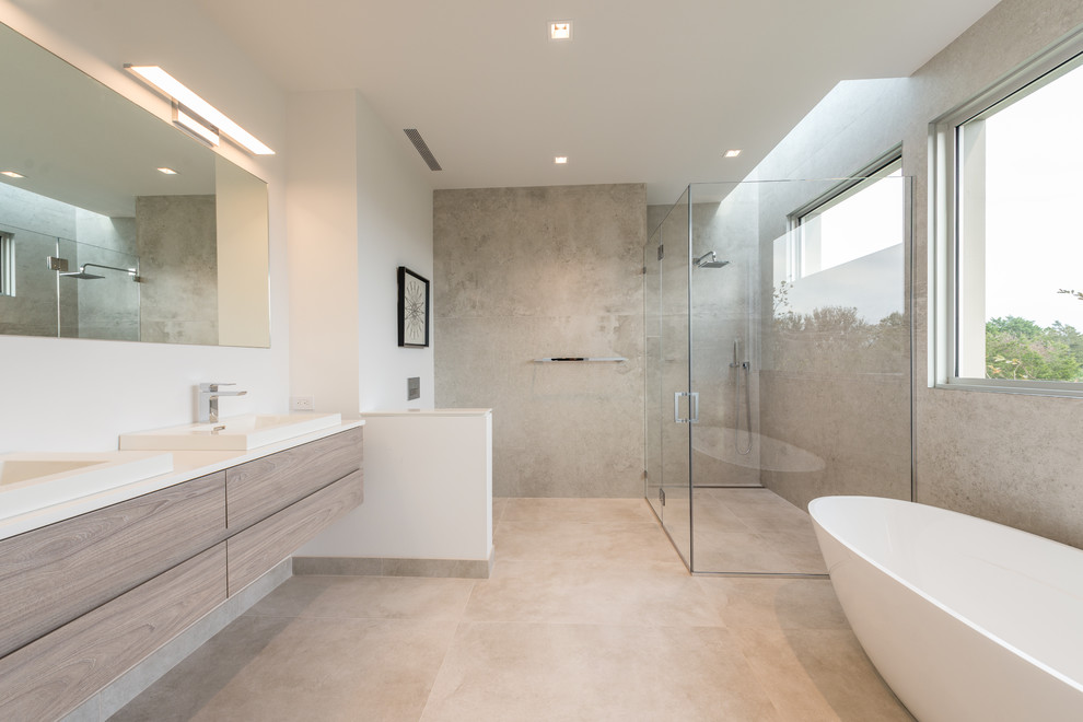 Design ideas for an expansive contemporary master wet room bathroom in New York with furniture-like cabinets, light wood cabinets, a freestanding tub, a wall-mount toilet, gray tile, porcelain tile, beige walls, porcelain floors, an integrated sink, beige floor and a hinged shower door.
