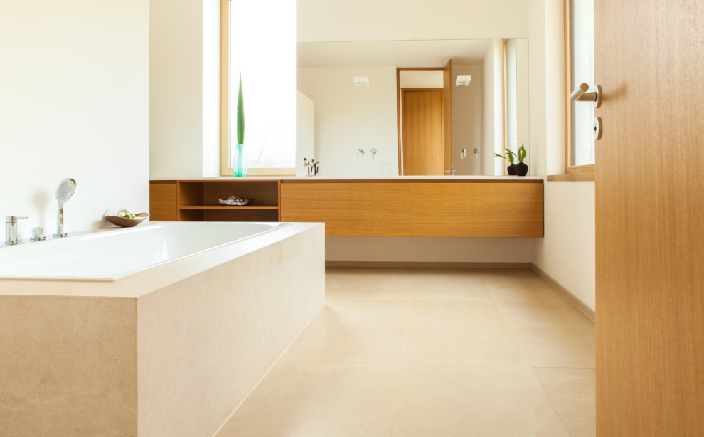 This is an example of a large contemporary bathroom in Other with flat-panel cabinets, light wood cabinets, a drop-in tub, a curbless shower, a two-piece toilet, beige tile, limestone, beige walls, limestone floors, an integrated sink, solid surface benchtops, beige floor, an open shower, white benchtops, a niche, a single vanity and a floating vanity.