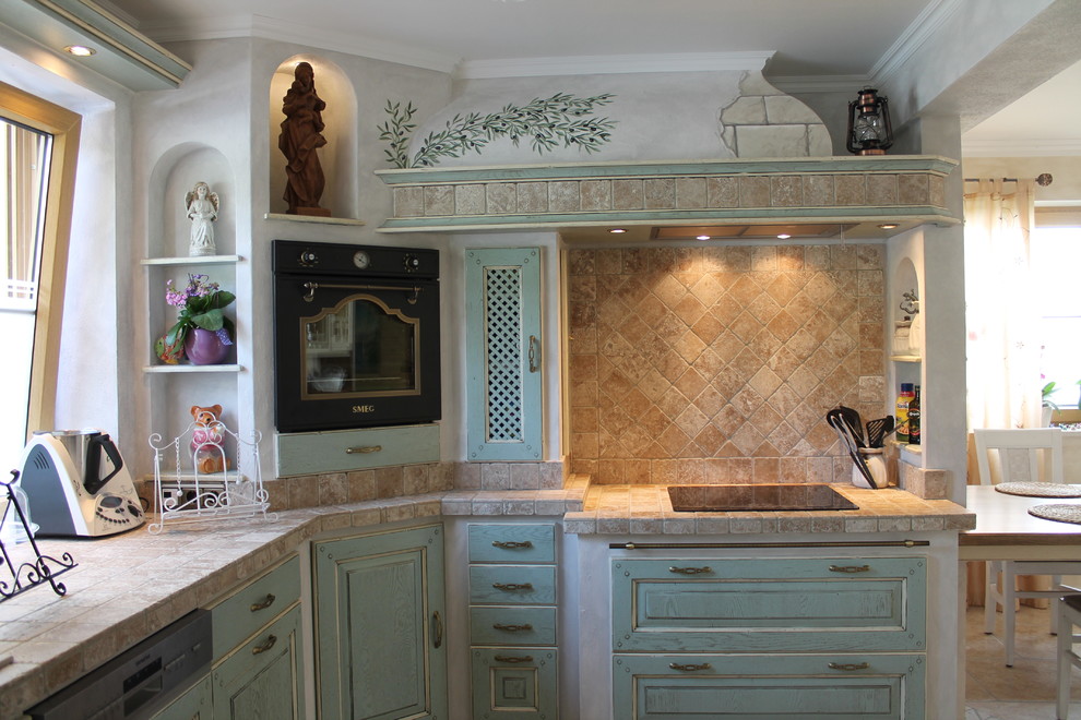 Design ideas for a large mediterranean l-shaped eat-in kitchen in Munich with a drop-in sink, beaded inset cabinets, turquoise cabinets, beige splashback, mosaic tile splashback, black appliances, terra-cotta floors, no island, beige floor and beige benchtop.