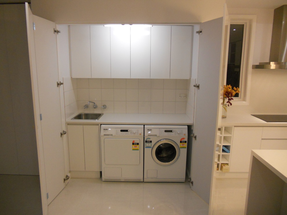 Small contemporary single-wall laundry cupboard in Melbourne with a single-bowl sink, flat-panel cabinets, white cabinets, laminate benchtops, white walls, porcelain floors and a side-by-side washer and dryer.