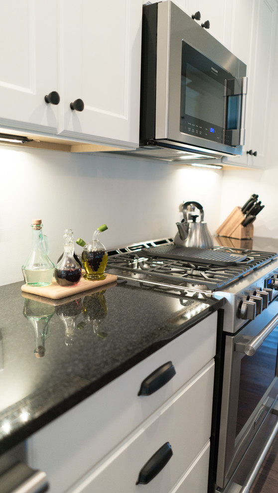Mid-sized transitional l-shaped dark wood floor open concept kitchen photo with an undermount sink, shaker cabinets, white cabinets, granite countertops, gray backsplash, stainless steel appliances and an island