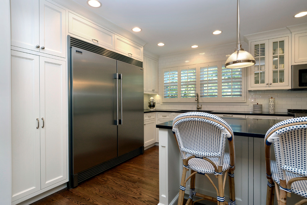 Example of a mid-sized transitional l-shaped dark wood floor and brown floor eat-in kitchen design in Chicago with white cabinets, granite countertops, white backsplash, subway tile backsplash, stainless steel appliances, an island, an undermount sink, recessed-panel cabinets and black countertops